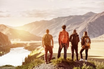 Four friends stand overlooking a sunset, mountains and river.