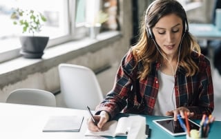 woman listening to podcast and taking notes